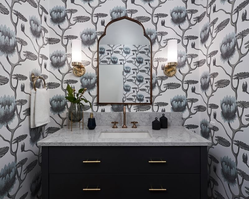 Powder bath remodel with black-and-blue botanical wallpaper, navy vanity, marble counter, and brass fixtures