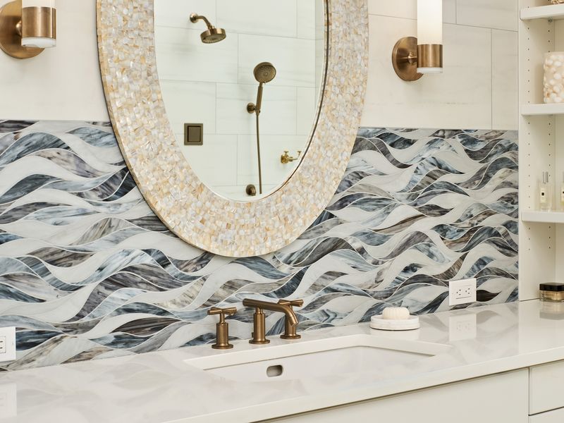 Vancouver coastal bath remodel with wave-pattern glass mosaic backsplash, mother-of-pearl mirror, and brass faucet