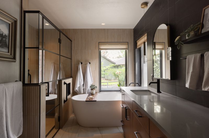 Warm contemporary Bend primary bath with freestanding tub, fluted tile walls, walnut vanity, and matte black fixtures