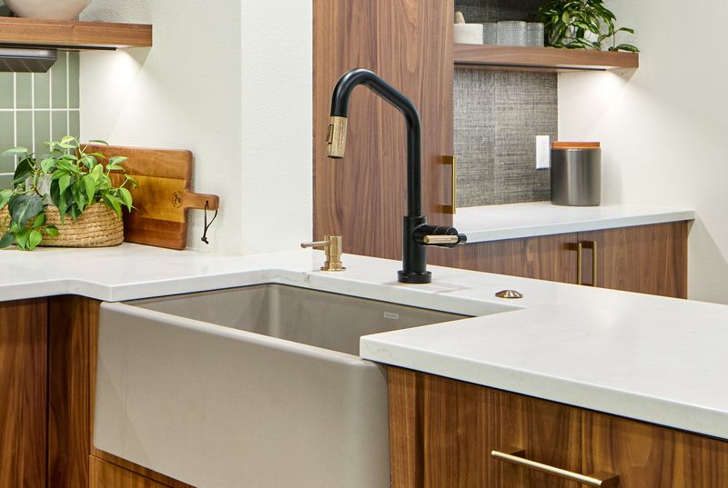 Walnut kitchen with concrete farmhouse sink, black and brass faucet, quartz counters, and sage green tile