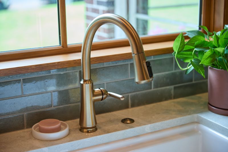 Kitchen sink with brushed nickel pull-down faucet, gray tile backsplash, and limestone counter at a window