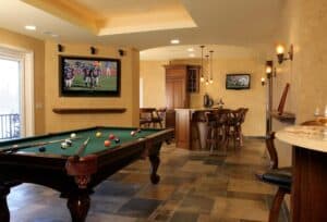 Man cave with pool table, television, bar, and natural lighting.