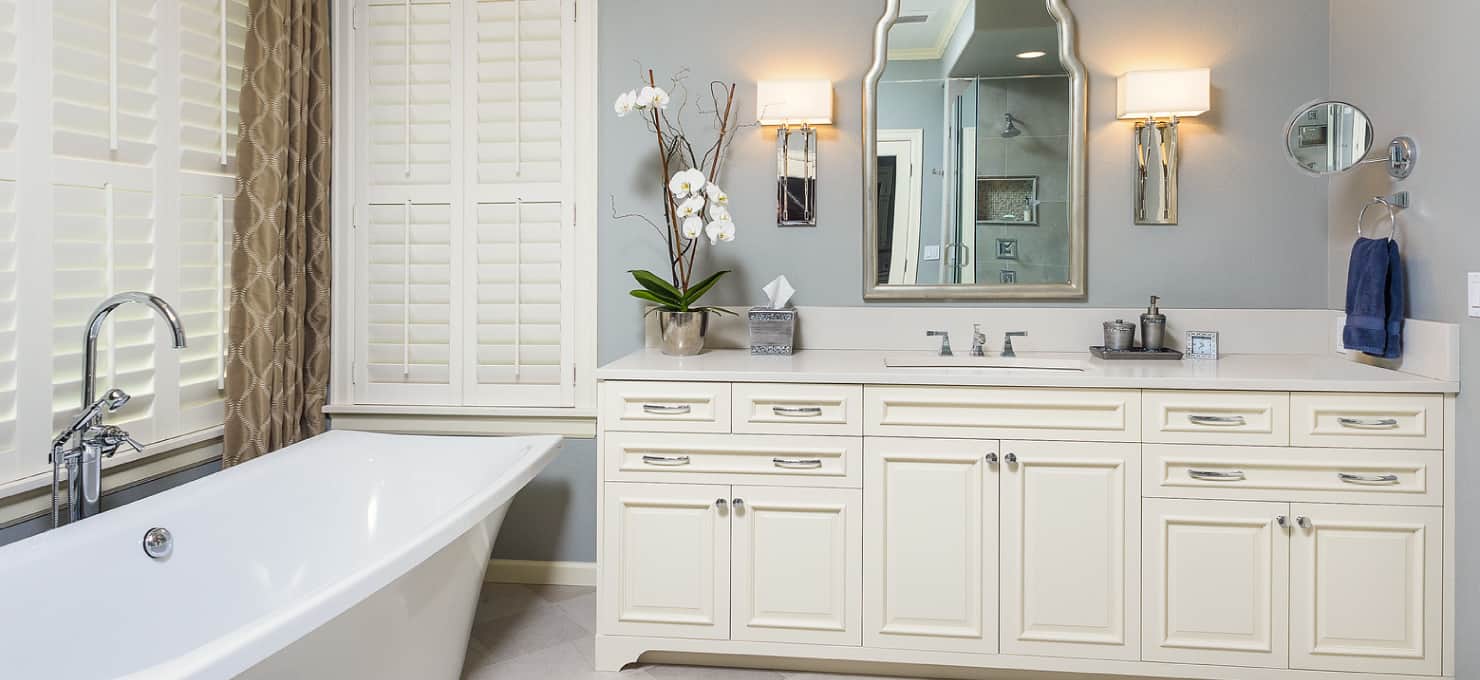 White, wooden vanity to the right of a white freestanding tub in a bathroom with light blue walls.