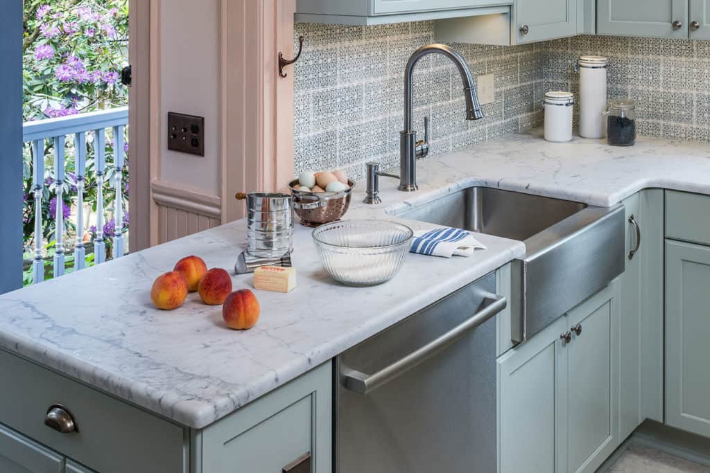 Kitchen with Carrara marble countertops, green cabinets, soft peachy walls, a faux tin ceiling, and an ornate tile backsplash from Pratt and Larson Tile.