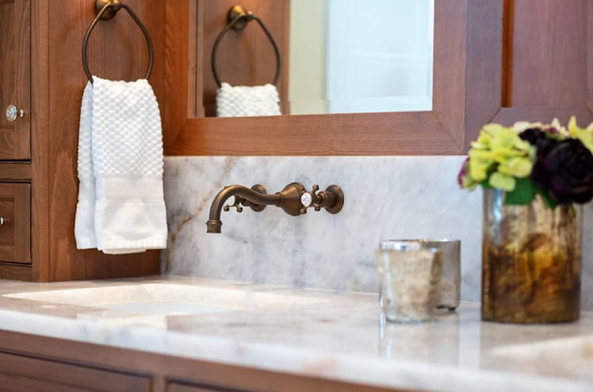 Bathroom sink with nob faucet handles, a granite countertop, and wood shelving and trim around the mirror.