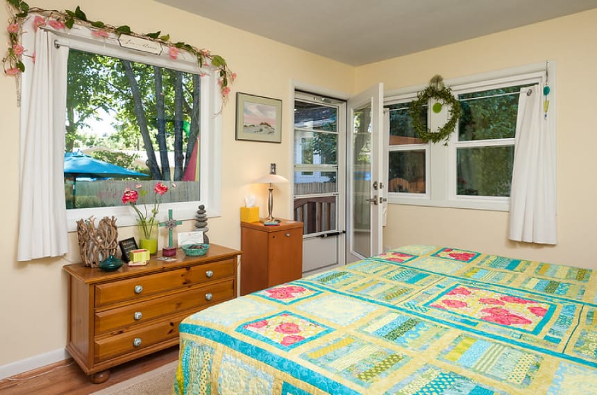 Guest room with a wooden dresser below the window and a queen-sized bed with a pastel-colored bed sheet.