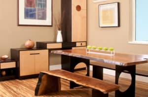 Contemporary park bench dining table in the center of a room with tan walls, contemporary art, and black and a tan armoire.