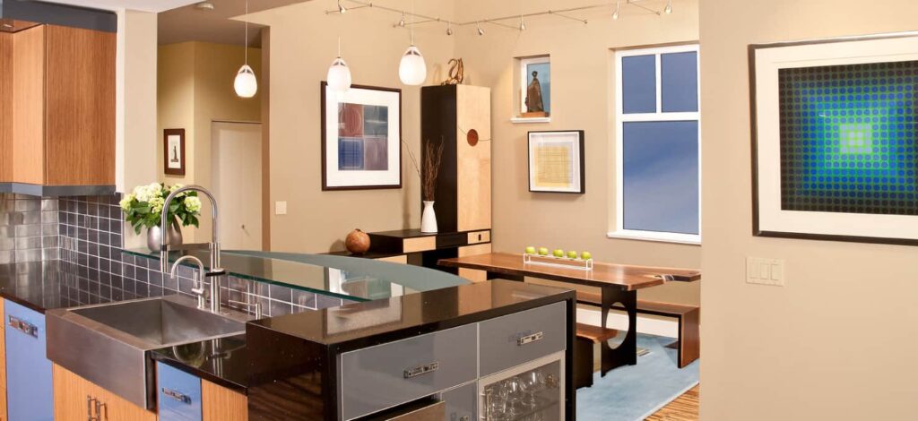 Contemporary kitchen overlooking a dining area with tan walls, table with wooden benches, and contemporary art on the walls.
