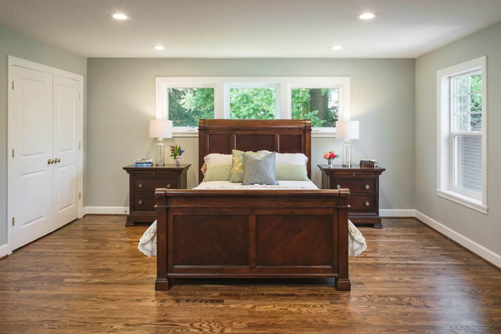 Traditional style master bedroom with oak hardwood floors, bed with wood head and foot boards, and two wood nightstands.