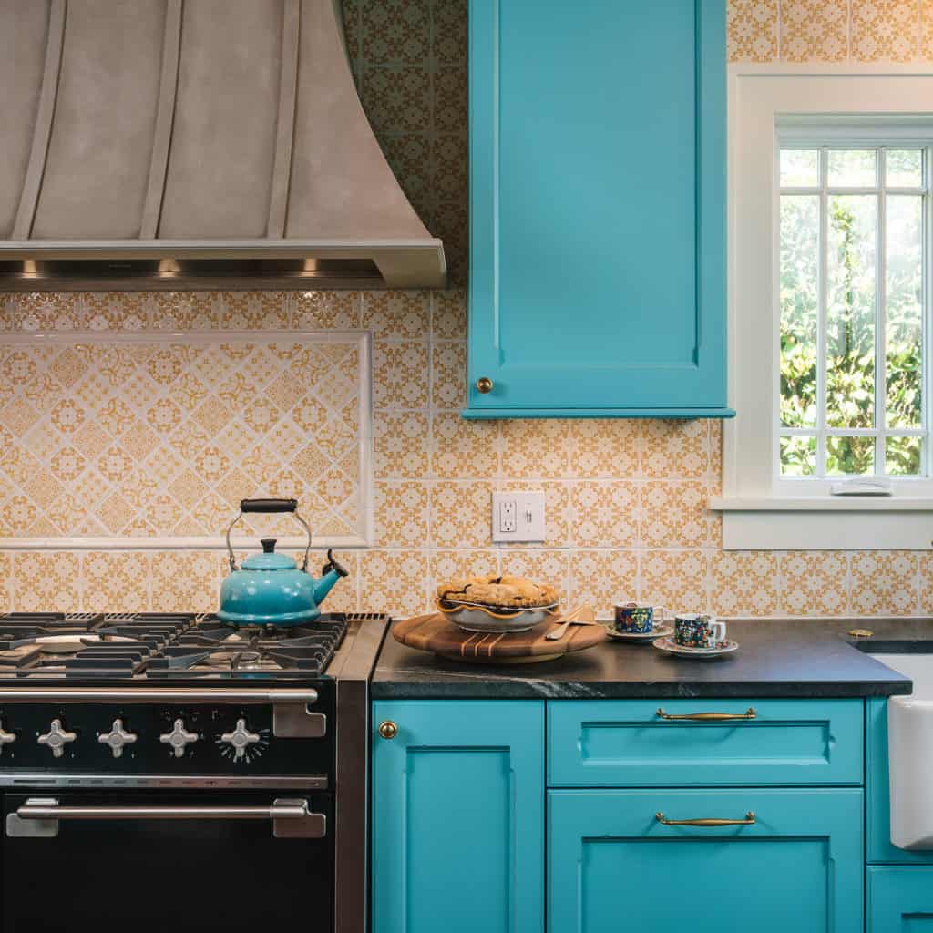 Orange and white graphic glossy tile above a kitchen stove with surrounding light blue cabinets and drawers.