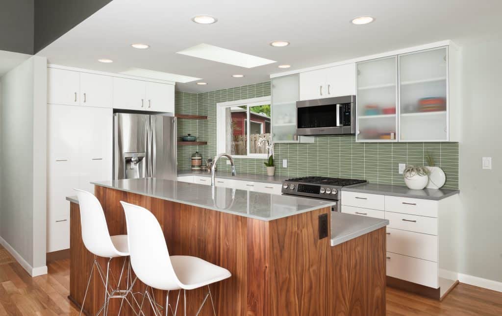 Geometric green backsplash tile in a contemporary kitchen with a wood-finished island and white cabinets and drawers.