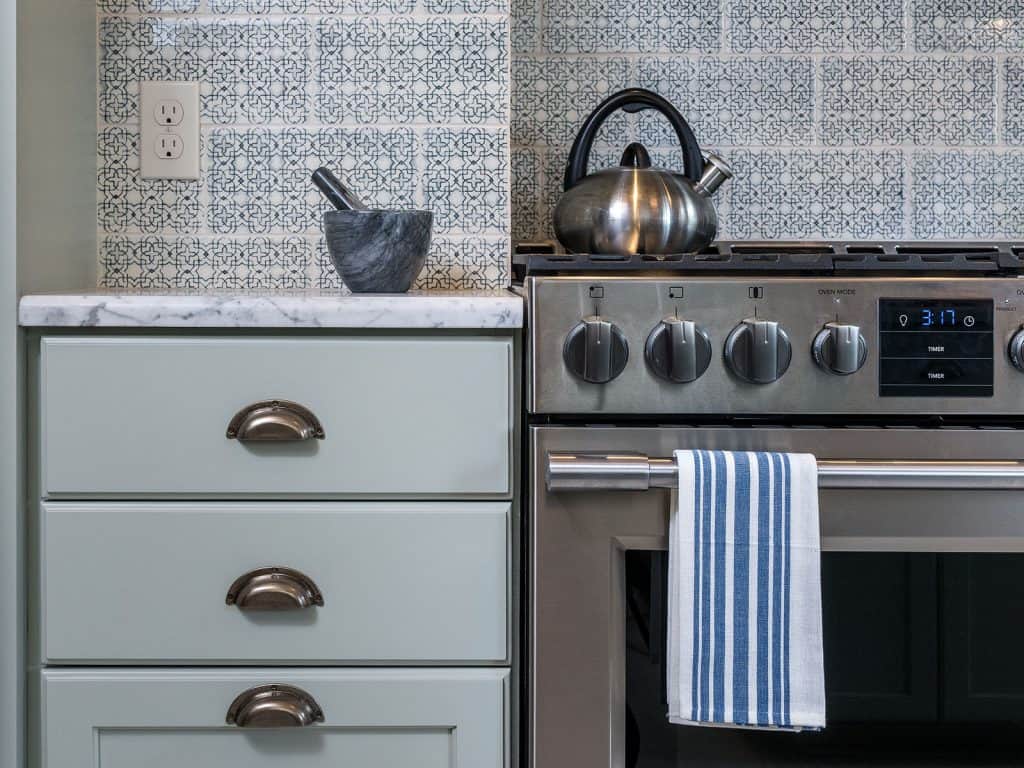 Tan and grey mosaic backsplash tile in a small modern kitchen with wooden cabinets and stainless steel appliances. 