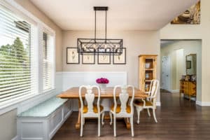 A modern kitchen features hints of traditional design, with hardwood flooring, wood cabinets, unique lighting fixtures, and a banquette.