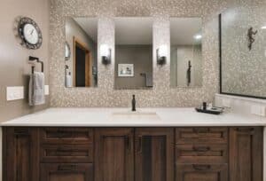 Dark wooden vanity with white countertop under three separated mirrors on a tile wall. 