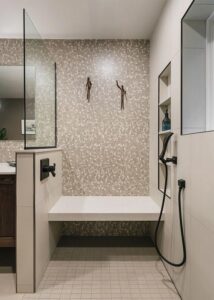 Tiled shower alcove with a black handheld shower head and quarts bench. 
