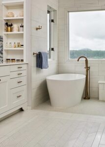 White freestanding bathtub next to white subway tile walls, beneath two windows.