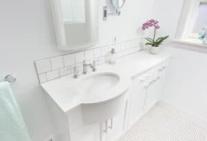 White vanity with white quartz countertop under a mirrored medicine cabinet.