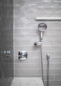 Stainless steel heard shower head on a light-grey subway tile wall. 