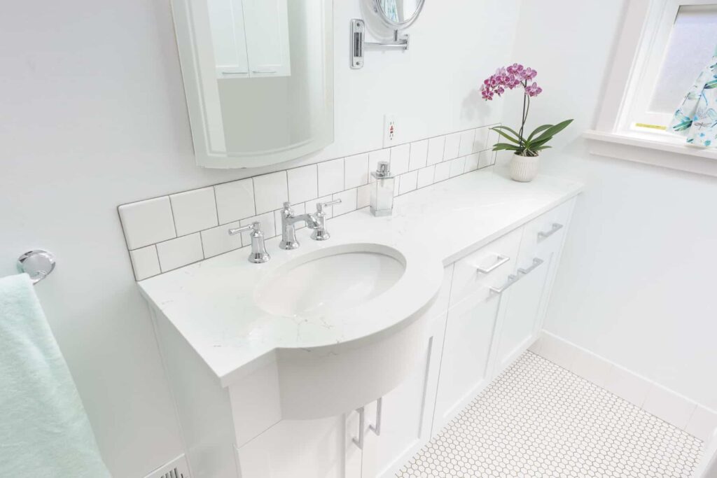 Single white basin sink over a white double vanity in a bathroom with tile floor next to a window.