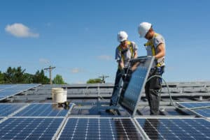 Two handymen installing solar panels in a row on top of a roof.