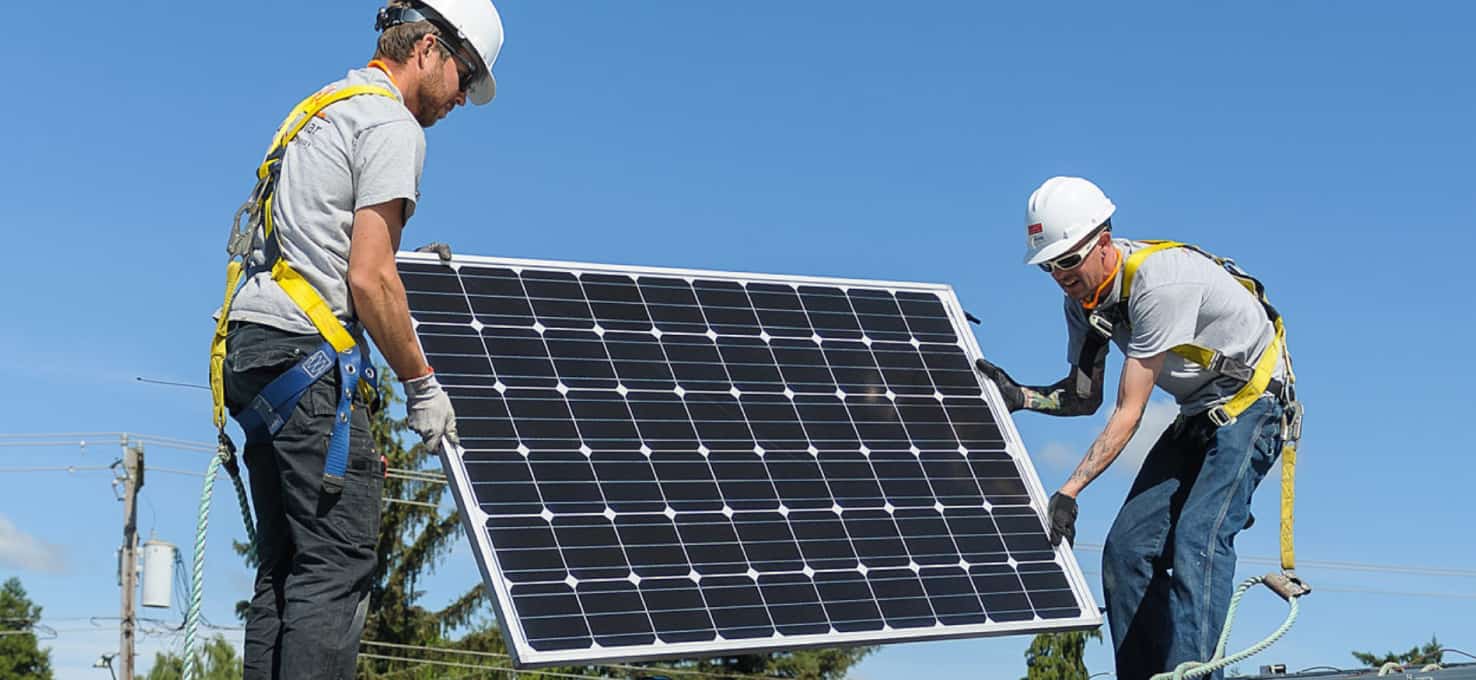 Two handymen installing solar panels on top of a roof.