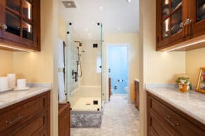 Entryway to a bathroom with a glass-enclosed shower, a grey bathmat, and light grey floor tile.