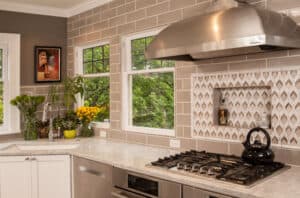 Gas stove with an aluminum hood in a modern kitchen with subway tile walls and quartz countertops.
