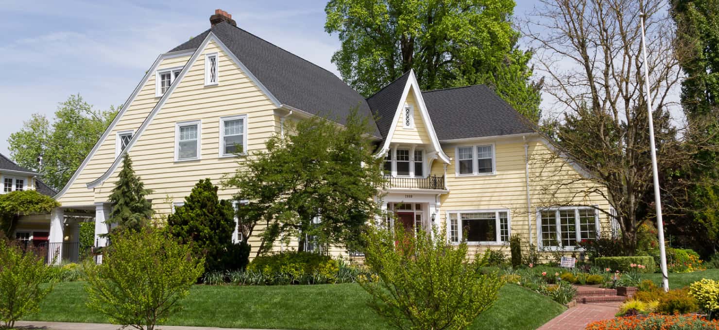 Yellow Victorian style two-story house with a red front door and a green-grass front lawn.