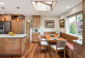 A wooden dining table with three pull-out chairs and an L-shaped banquette up against the wall corner.