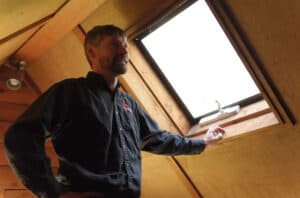 man standing by closed window in attic space.
