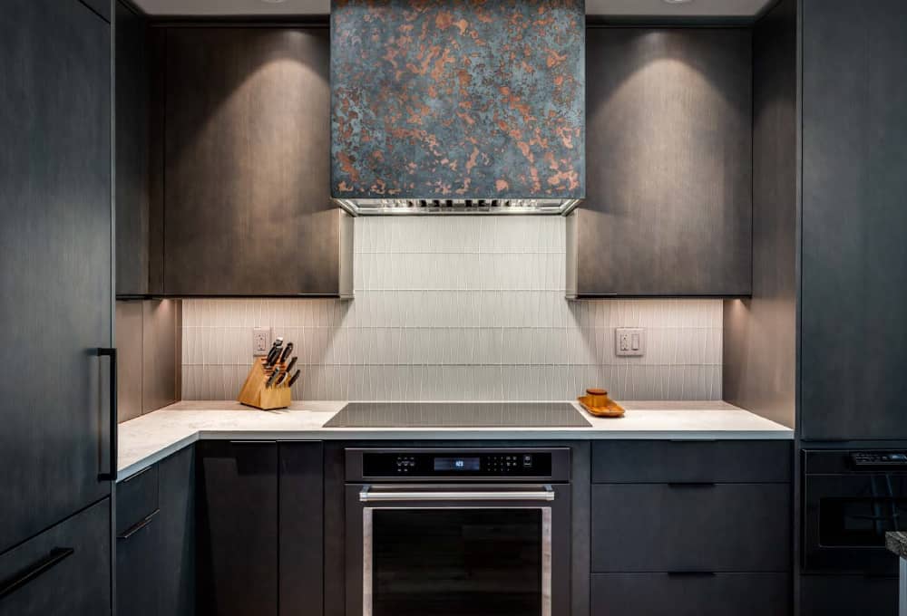 Black electric stove top built into Imagine Stoneworks countertops with a hood vent and dark-stained cabinets above.