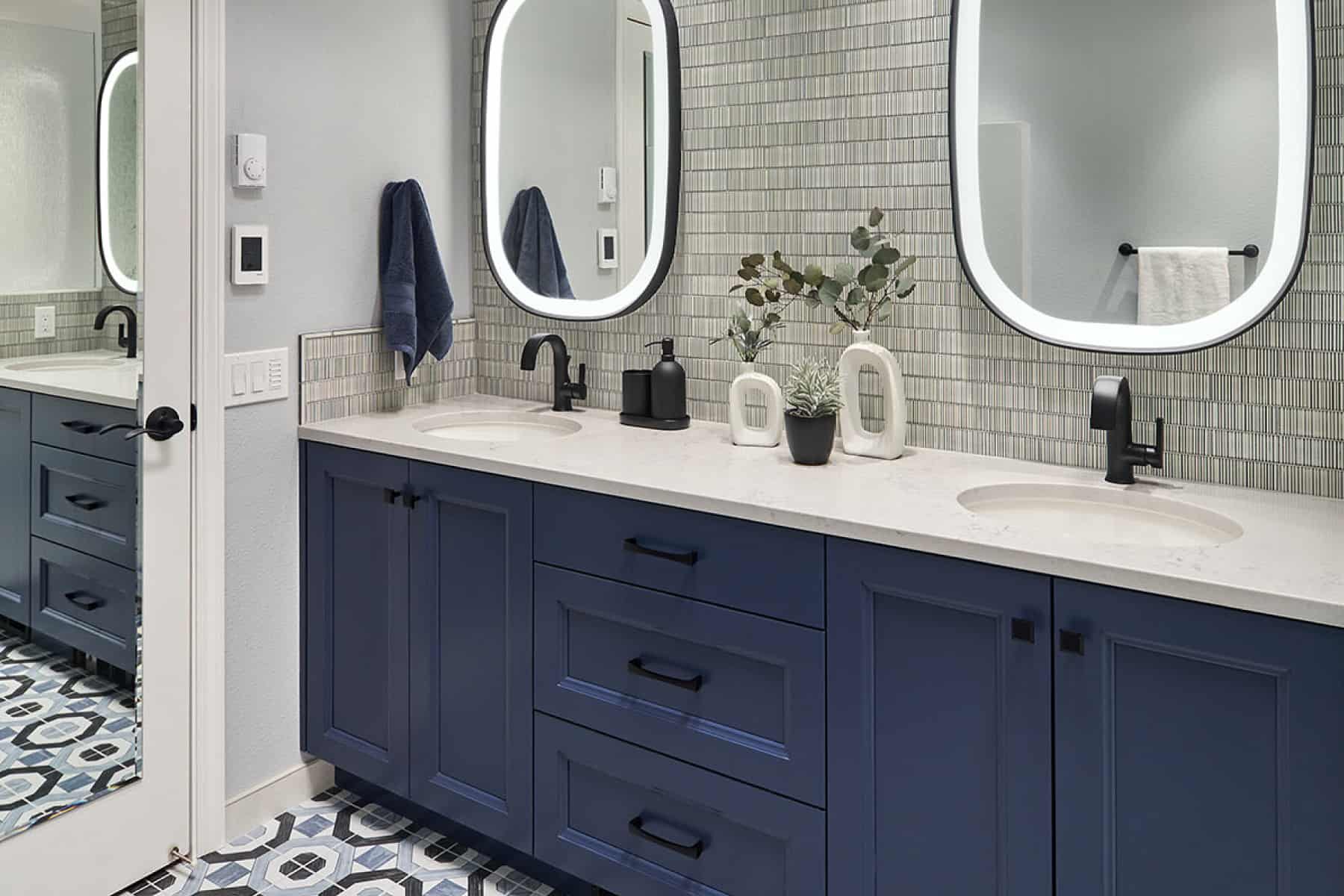 Dual LED lighted vanity mirrors above a double vanity with quartz countertops and deep blue cabinetry from Decor Cabinets.