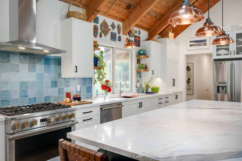 Bright, modern kitchen featuring white cabinetry, a large marble island, copper pendant lights, and colorful wall decor.