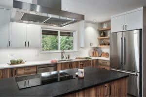 Stylish modern kitchen featuring a sleek island with a dark countertop, stainless steel appliances, wooden accents, and a window view of greenery.