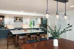 Contemporary kitchen with a spacious island, dark cabinetry, stylish pendant lights, and a dining area featuring a wooden table and a potted plant.