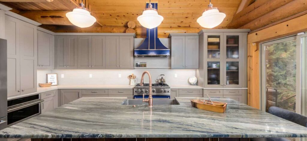 Modern kitchen featuring gray cabinets, a blue hood, a large marble island, and wooden beams, creating a cozy and stylish atmosphere.
