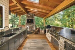 Spacious outdoor kitchen featuring stainless steel grills, a stone fireplace, and a cozy seating area under a wooden roof.