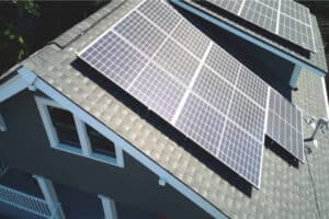 An aerial view of a house roof featuring several solar panels installed, with a slanted roof design and balcony visible.