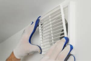 Person wearing gloves installing a white vent cover in a bathroom.