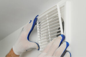 Person wearing gloves installing a white vent cover in a bathroom.