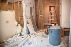 Room demolition with crumbling walls, debris on the floor, and construction tools and ladder.