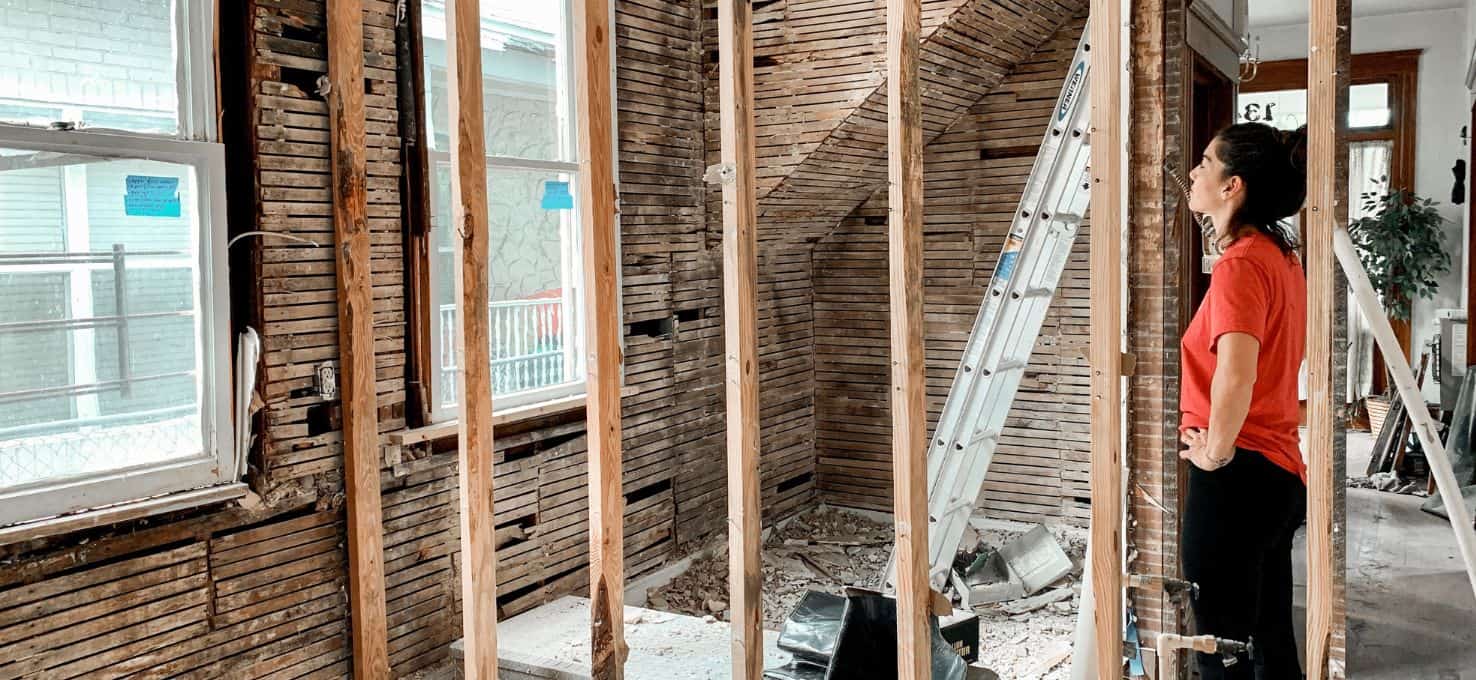 Woman inspecting a room under renovation with exposed studs and construction debris.