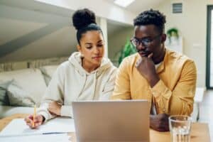 A woman and man sitting at a table looking at a laptop.