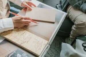 A person writing in a notebook on a glass coffee table.