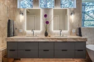 A modern double vanity bathroom with two mirrors, rectangular sinks, and dark gray drawers beneath a light stone countertop.