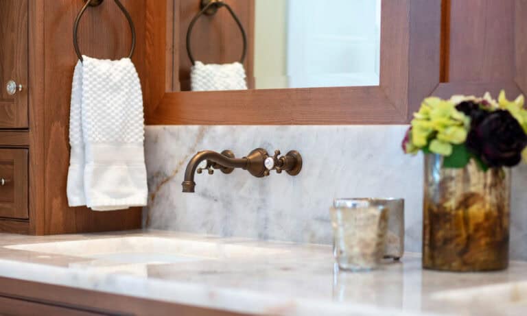 Wall-mounted bronze faucet and white marble countertop in a luxury bathroom.)