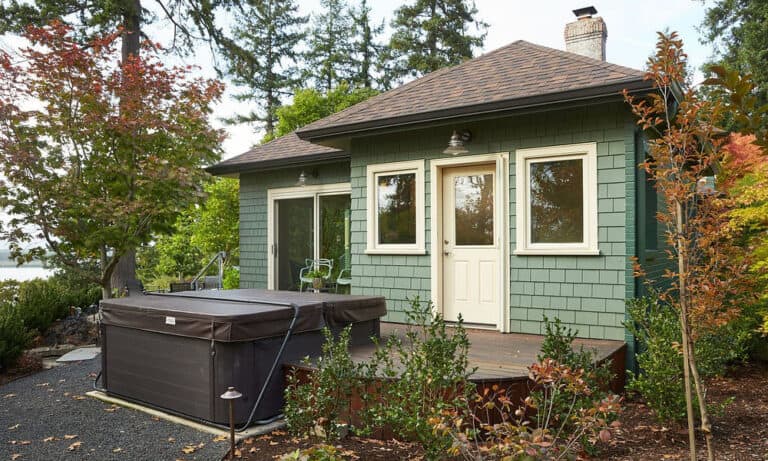Lakeside cottage with a detached hot tub and green shingle siding.)