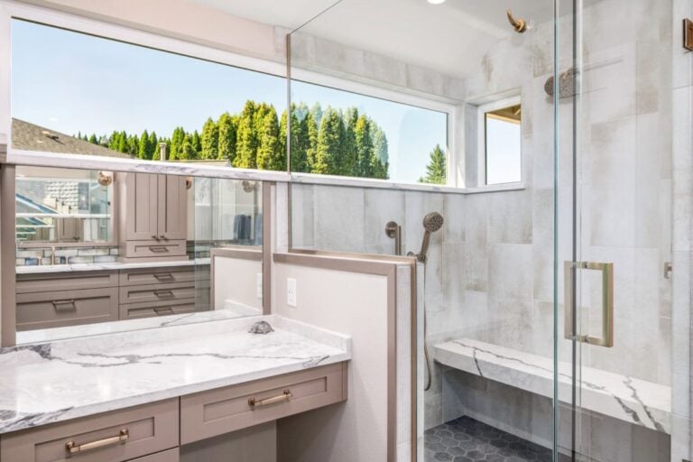 Luxurious modern bathroom with marble countertops, glass shower, and bright natural light.