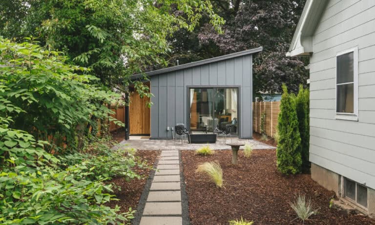 Backyard AD with a glass door, patio seating, and a minimal landscaped path.)