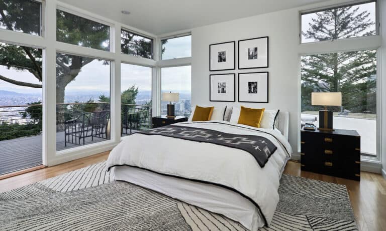 Modern bedroom with panoramic windows, a plush white bed, and a scenic balcony view.)